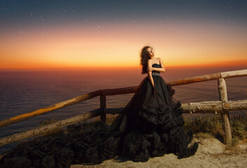 beautiful brunette girl in a black long dress on a mountain cliff overlooking the sea.