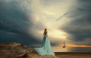 Fototapeta na wymiar девушка в голубом платье на закате смотрит на море с парусным кораблём.