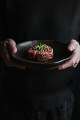 eef tartare on a dark plate in the hands of a man