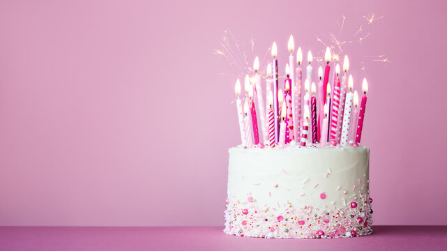 Pink birthday cake with many pink birthday candles and sparklers