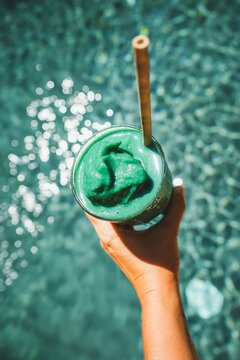 hand holding a glass green smoothie healthy pool lifestyle