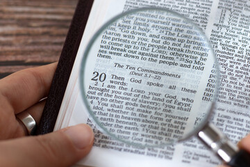 Human hand holding a magnifying glass over open holy bible book of Exodus verses for Ten...