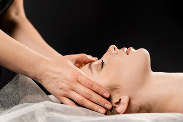 Fototapeta na wymiar Girl with closed eyes is relaxing on face and neck massage in spa. Masseur is making facial massage for young woman in spa. Facebuilding and relaxing procedures.