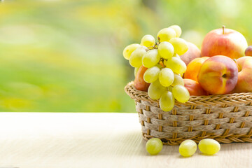 Fresh ripe apples, peaches, green and blue grapes in basket. Healthy food on table on defocus autumn background.