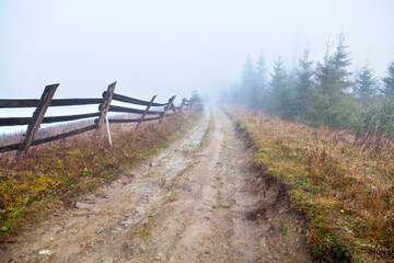 Autumn in the mountains, muddy road along a wooden fence, fog in the background. Ukraine, Carpathians.