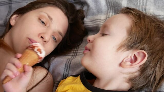 A young woman and a little boy eat an ice cream cone together lying