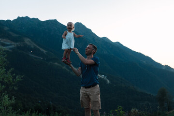a young father holds his daughter against the backdrop of mountains. The concept of happy fatherhood and father's day.