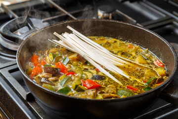 A frying pan with stewed vegetables in sauce and spices contains udon.