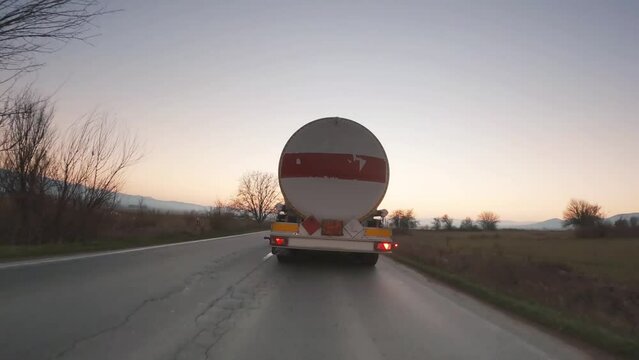Rear view of white cistern truck driving fast on highway at sunset
