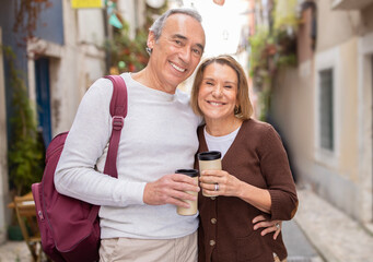 Happy Mature Spouses Embracing Holding Coffee Cups Standing In Lisbon