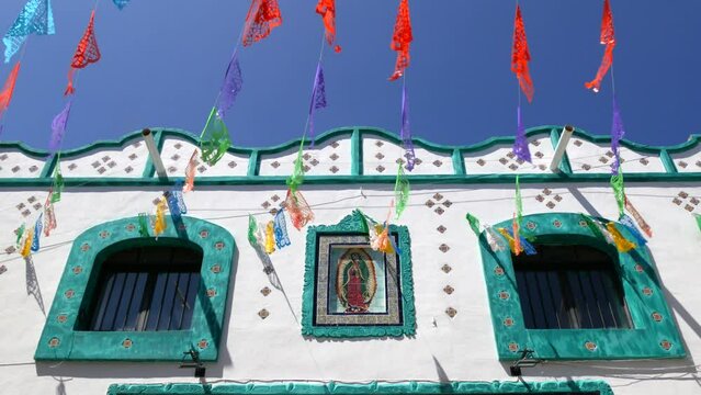 Mexican building with an image of the Virgin of Guadalupe. Colorful mexican perforated papel picado banner, festival colourful paper garland.