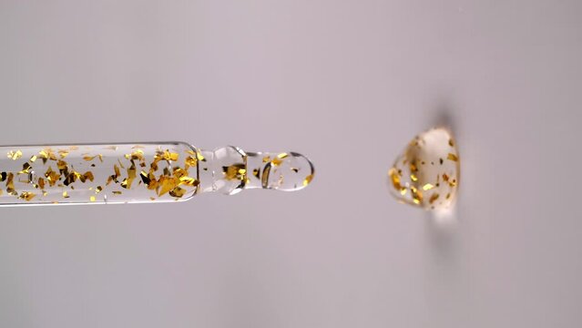 Liquid gel or serum with gold particles drips from a pipette, vertical format. Slow motion.