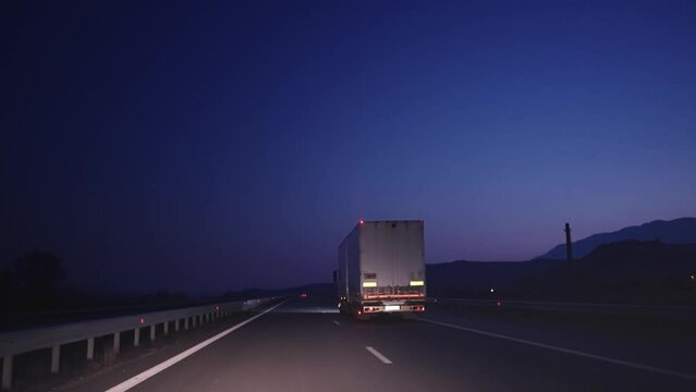 Follow shot of truck with cargo trailer driving on the busy highway in the rural region at night, transportation delivery concept, slow motion