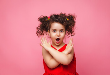 emotional portrait of a little girl in a red dress on a pink background.