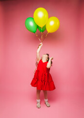 Portrait of a cheerful little girl isolated on a pink background, holding a bunch of colorful balloons, posing.