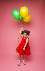 Obraz na płótnie Canvas Portrait of a cheerful little girl isolated on a pink background, holding a bunch of colorful balloons, posing.