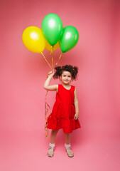 Obraz na płótnie Canvas Portrait of a cheerful little girl isolated on a pink background, holding a bunch of colorful balloons, posing.
