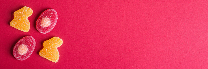 Jelly Easter sweets in form of bunny and egg in orange, red and yellow colors on pink-red cardboard background. Easter card, copy space, selective focus.