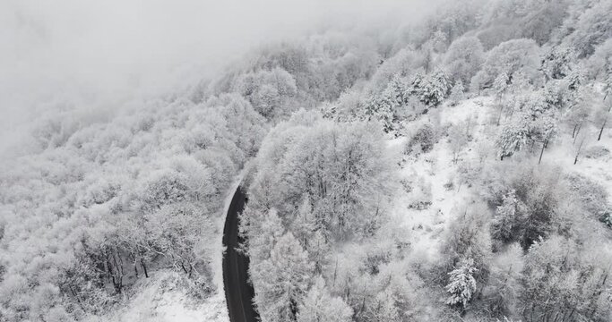 Aerial view of car vehicles driving on curvy windy road with snow mountain landscape and snow covered forest, cinematic view