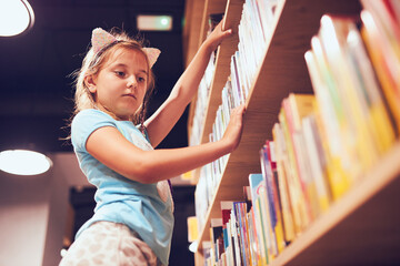Schoolgirl looking for book in school library. Student choosing book for reading. Learning from books. Back to school. Elementary education. Doing homework