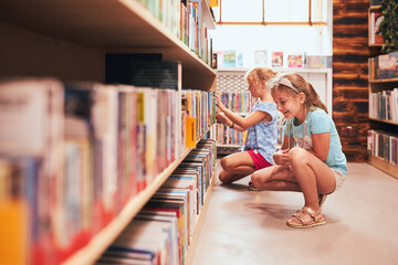 Two schoolgirls choosing books in school library. Primary school students learning from books. Children having fun in school club. Back to school