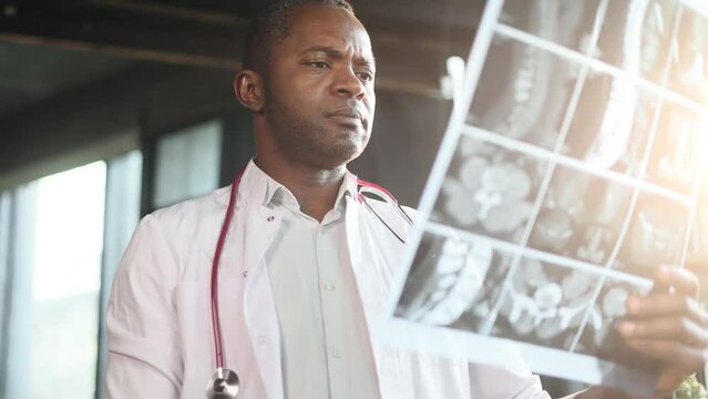 Portrait of unhappy mature african american man doctor therapist looking at bad negative results patient MRI or CT scan procedure and looking at camera with thumbs down at light hospital office