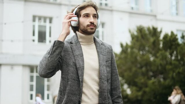 Successful inspired arabian businessman with headphones listen to music and relaxing in the modern city centre Handsome young muslim man entrepreneur looking ahead outdoors alone