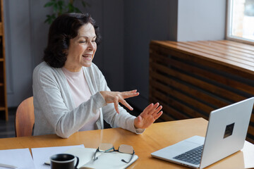 Happy middle aged senior woman sit with laptop talk on video call with friends family. Laughing mature old senior grandmother having fun talking speaking with grown up children online