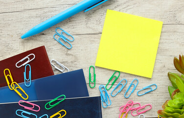 Office desk with yellow sticker, blue pen and colorful paper clips. Concept of remote office and work from home. Top view flat lay with copy space