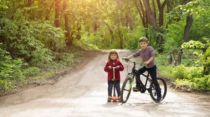 kids brother and sister ride a bike and scooter in the park. copy space