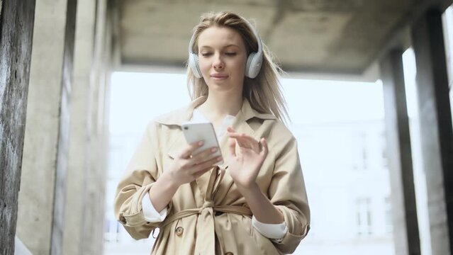 Successful young blond businesswoman listen to music hold smartphone scrolling social media texting browsing online and looking at camera in modern business centre Communication and network concept 