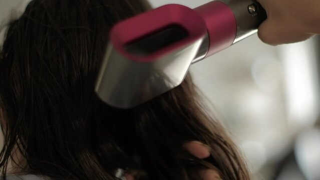 Young brunette woman dries hair on back of head with electric hair dryer