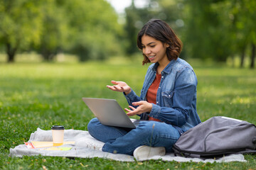 Naklejka na ściany i meble Smiling arab female student making video call on laptop outdoors
