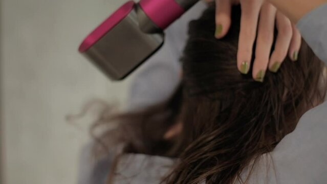 A young woman dries hair with an electric hair dryer in front of a mirror