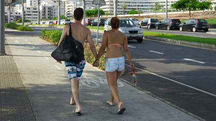 Honeymoon in Madeira. A young married couple in beachwear returns from the beach to the hotel. The woman is holding a bouquet. Funchal cityscape..