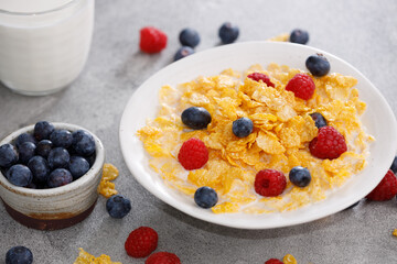 Delicious corn flakes garnished with raspberries and blueberries on a gray background for a hearty breakfast.