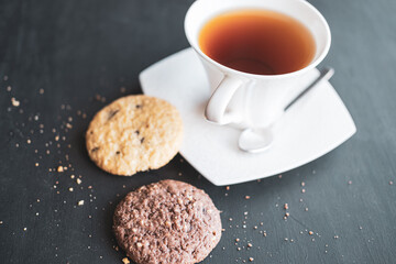 Two cookies with a cup of black tea on black background, brown cookies with afternoon tea concept.