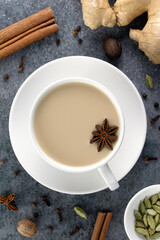 Obraz na płótnie Canvas Indian masala tea in a white mug with spices - cinnamon, star anise, ginger, cloves, cardamom on a gray background.