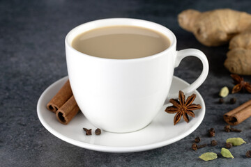 Indian masala tea in a white mug with spices - cinnamon, star anise, ginger, cloves, cardamom on a gray background.