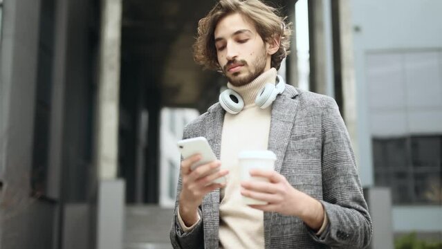 Successful young arabian muslim businessman with cup of coffee hold smartphone scrolling social media texting browsing online checking email in modern business centre 