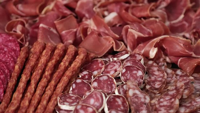 Meat plate with assortment of various tasty Spanish, french or Italian appetizers - sliced prosciutto, sausage, salami, kabanos sausages, fuet. Meat platter rotating
