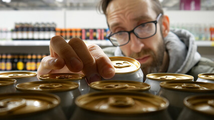Close-up of many golden white cans of beer on a store shelf and a man reading the product...