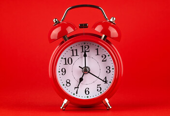 Red alarm clock on a red background. It's 7 o'clock on the clock. Morning. 