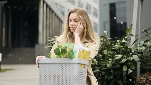 Portrait of fired sad blond businesswoman carries box with personal belongings leaving the office centre Pensive woman looking at person who hurry to work thinking about future after unemployed