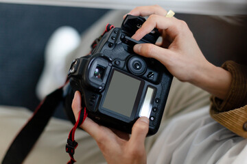 Rear view of male photographer holding camera working with photos, looking through taken pictures, blank screen mockup