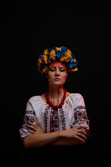 portrait of a girl in Ukrainian national clothes and jewelry with a wreath of blue and yellow flowers, closed eyes, blood on her face as a symbol of the war in Ukraine on a black background, vertical