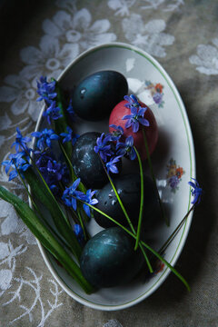 Happy Easter! Easter naturally painted eggs on plate with blue bluebell flowers on rustic table.