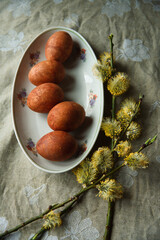 Happy Easter! Easter naturally painted orange eggs on plate with flowering willow tree branches on rustic table.