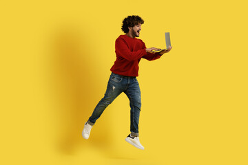 Fototapeta na wymiar Excited hindu guy using laptop and jumping up