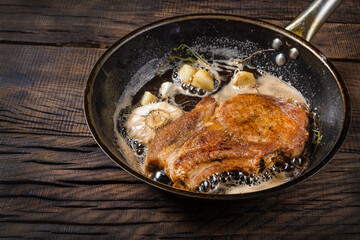 fried pork steak with seasonings in a frying pan, on a dark wooden background